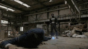 a man in a suit is laying on the floor in front of a superhero in a black suit