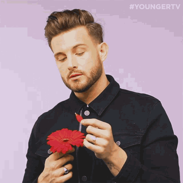 a man in a black jacket holds a red flower in his hands