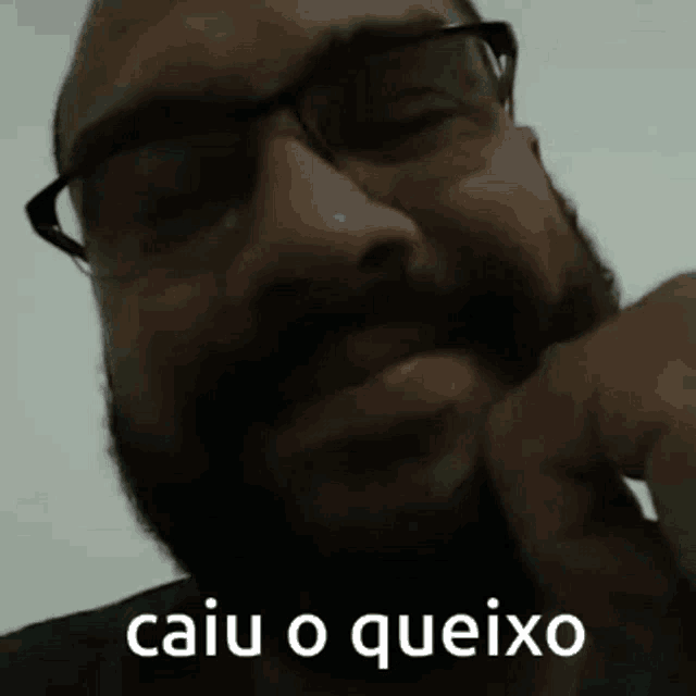 a man with glasses and a beard has the words caiu o queixo on his face .