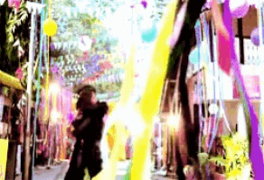 a woman is walking down a street with balloons and flags hanging from the trees