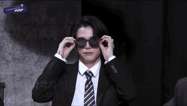 a man in a suit and tie adjusts his sunglasses in front of a sign that says " friendship map "
