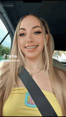 a woman with braces on her teeth is sitting in a car and has a tiktok on her phone