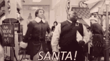 a black and white photo of a man standing in a store talking to a man in a santa suit .