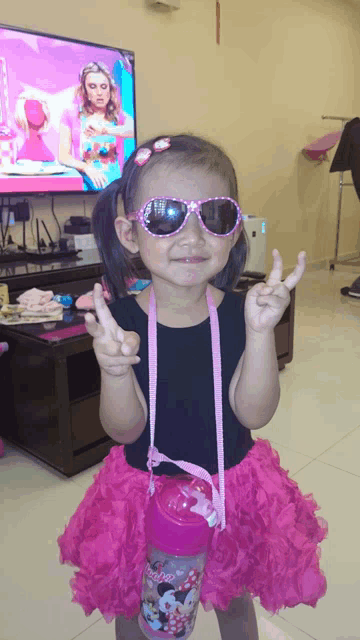 a little girl wearing sunglasses and a minnie mouse water bottle giving the peace sign