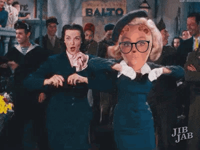 two women are dancing in front of a crowd in a movie .