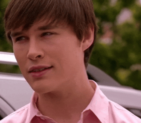 a young man wearing a pink shirt is looking at the camera