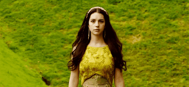 a woman in a yellow dress and headband is standing in a field .