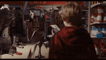 a boy in a red hoodie stands in front of a store with a sign that says bargains on it