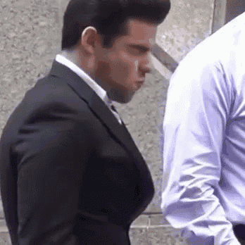 a man in a suit is standing next to another man in a blue shirt