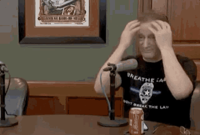 a man is sitting at a table in front of a microphone holding his head .