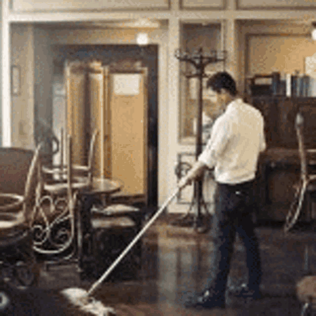 a man is mopping the floor in a room with tables and chairs