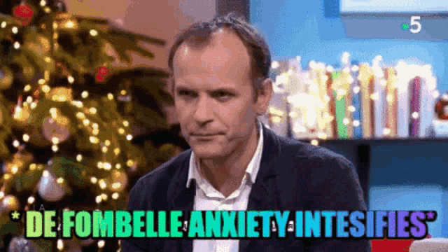 a man is sitting in front of a christmas tree with the words de fombelle anxiety intesifies