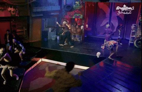 a group of people are dancing in front of a sign that says drag queen 2 on it