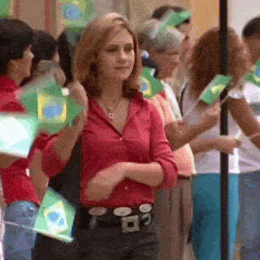 a woman in a red shirt stands in a crowd holding flags