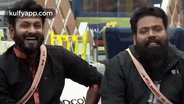 two men with beards are sitting next to each other in a room and smiling .