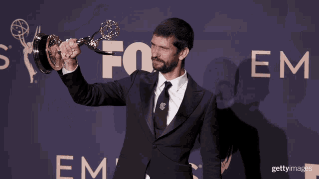 a man in a suit holds up a trophy in front of a fox em sign