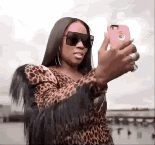 a woman wearing sunglasses and a leopard print jacket is taking a selfie with her cell phone .