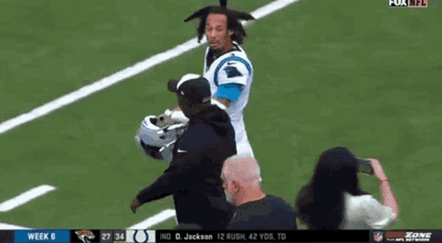 a man is standing on a football field talking to a player .