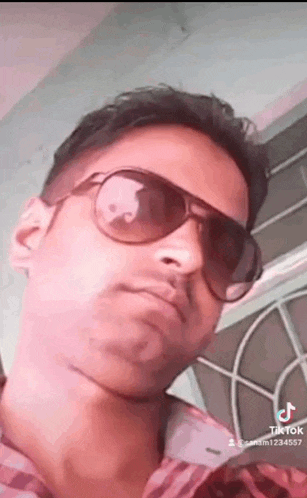 a young man wearing sunglasses and a plaid shirt is taking a selfie .