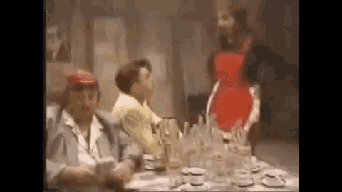a group of people are sitting at a table with a woman in a red apron standing behind them .