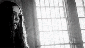 a black and white photo of a woman looking out of a window .