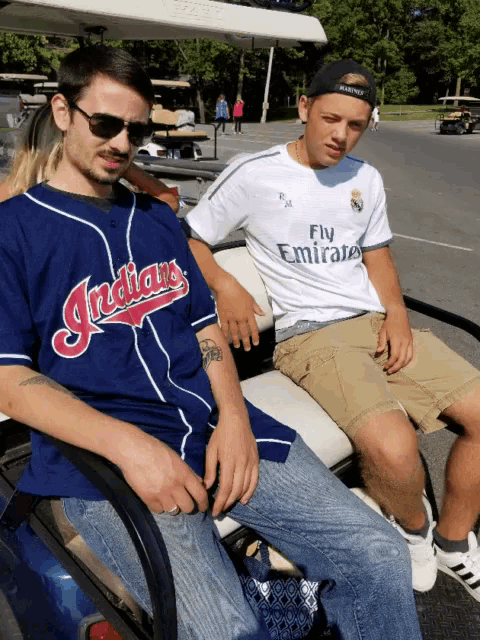 a man in a blue indians jersey sits next to a boy in a fly emirates shirt