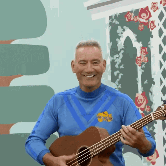 a man in a blue shirt that says the wiggles on it is playing a guitar