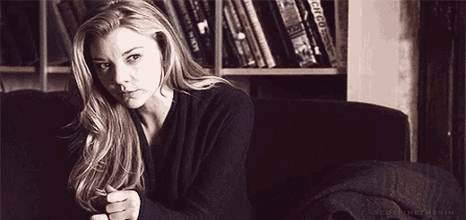 a woman is sitting on a couch in front of a bookshelf with books on it .