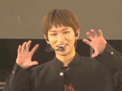 a young man wearing a black jacket and a microphone has his hands up