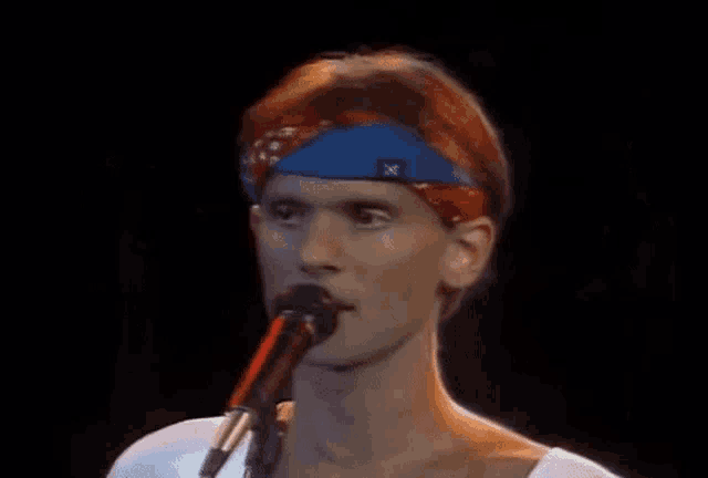 a man singing into a microphone with a blue headband on his head