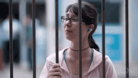 a woman with glasses and ear buds is behind bars .