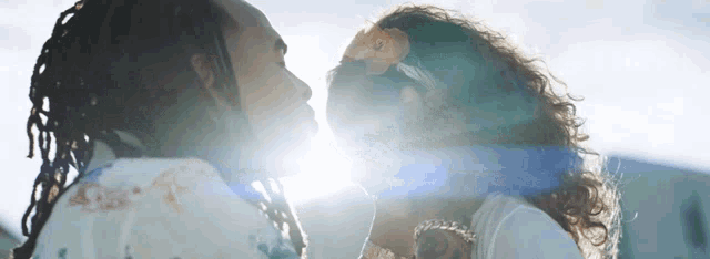 a man and a woman are kissing with the sun shining behind them