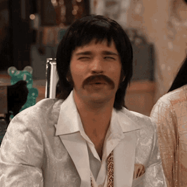 a man with a mustache wearing a white jacket and tie