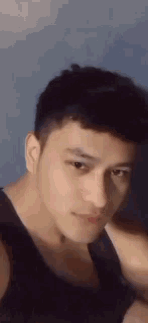 a young man in a black tank top is taking a selfie with his hand on his head .
