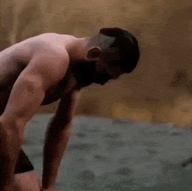 a shirtless man is standing on a beach with his head on his knees .