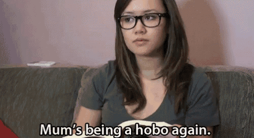 a woman wearing glasses is sitting on a couch and saying mum 's being a hobo again