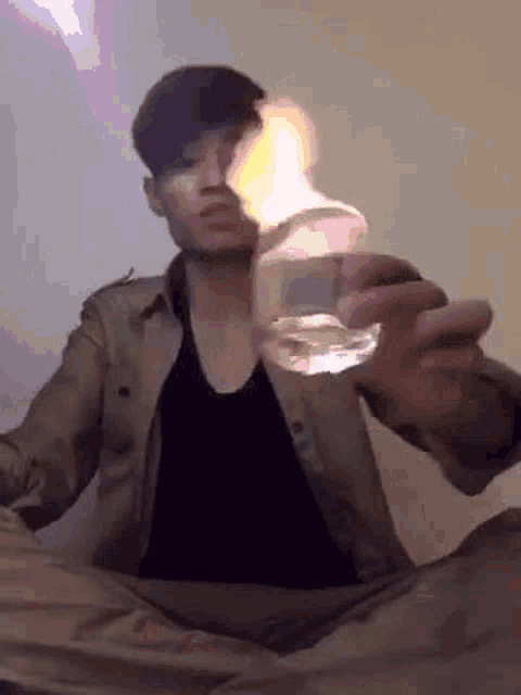 a man is sitting on the floor holding a glass of water with a fire coming out of it .