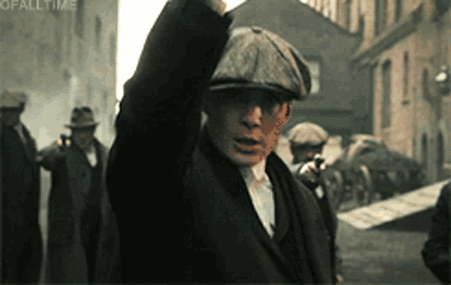 a man wearing a hat is walking down a street with his hand up