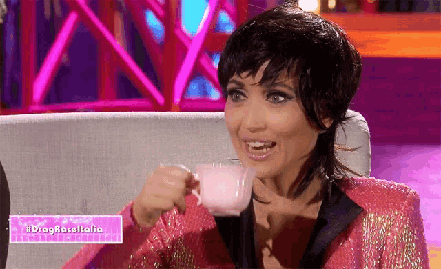 a woman in a pink jacket is drinking from a pink cup with the hashtag #dragraceitalia
