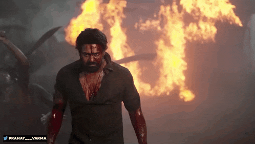 a man with blood on his face is standing in front of a fire with the hashtag pranay_varma on the bottom