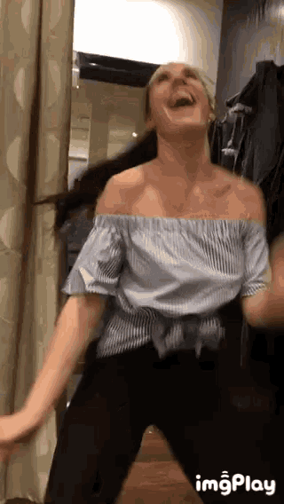 a woman in a blue off the shoulder top and black pants is dancing in a room .