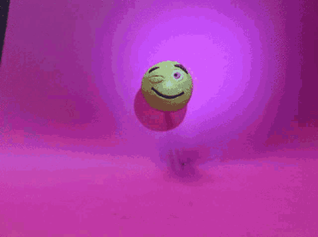 a yellow ball with a smiley face on it on a pink surface