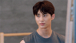 a young man in a gray tank top is standing in a gym and looking at the camera .