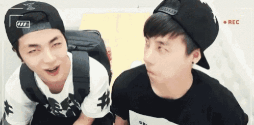 two young men wearing hats are standing next to each other and making funny faces .