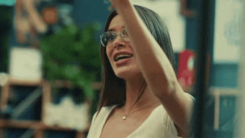 a woman wearing glasses and a white shirt is smiling with her arm up