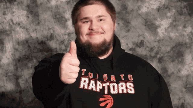 a man wearing a black toronto raptors sweatshirt gives a thumbs up