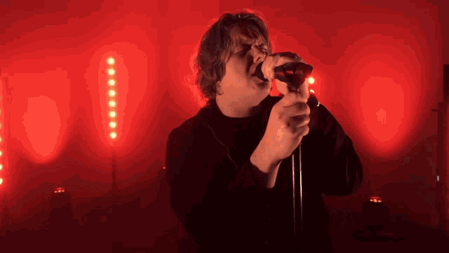 a man is singing into a microphone in front of red lights