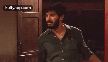 a man with a beard is standing in front of a door and looking at the camera .