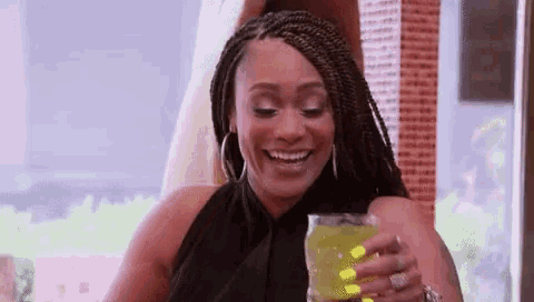 a woman in a black dress is holding a glass of green liquid and smiling .