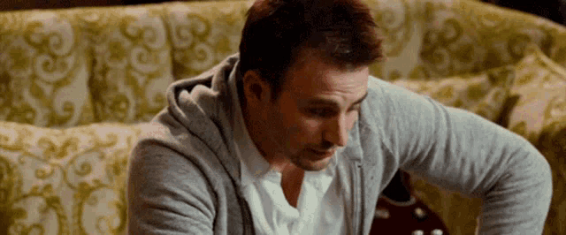 a man is sitting on a couch wearing a gray hoodie and a white shirt .